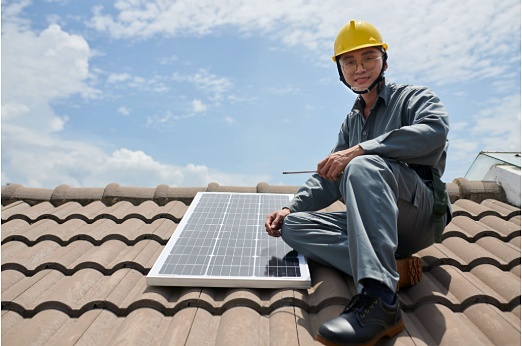 Juruteknik solar memakai topi keselamatan memeriksa panel solar di atas bumbung kediaman di Malaysia